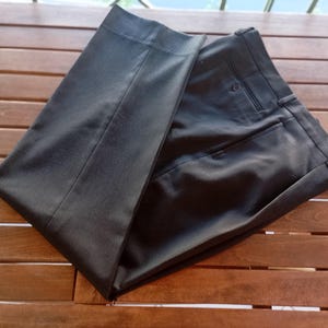 May include: A pair of dark charcoal grey dress trousers featuring a structured waistband with belt loops, a single visible button closure, and a clean, pressed front crease. The fabric has a smooth, matte finish with tailored seams.