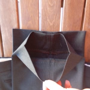 May include: A pair of black trousers featuring a straight leg design with a clean hemmed finish. The fabric is a solid black material with visible stitching along the interior seams of the leg opening, showcasing the construction of the garment.