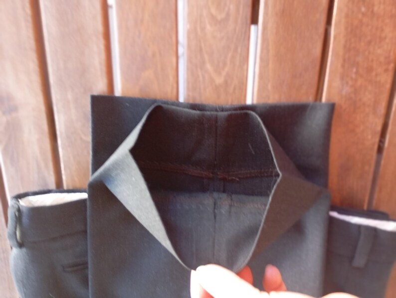 May include: A pair of black trousers featuring a straight leg design with a clean hemmed finish. The fabric is a solid black material with visible stitching along the interior seams of the leg opening, showcasing the construction of the garment.