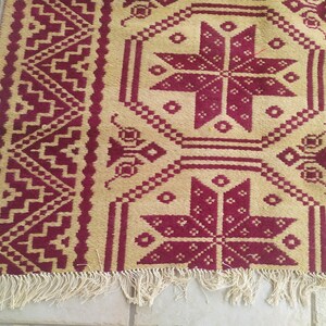 May include: A beige and burgundy rug with a geometric pattern. The rug has a fringed border.