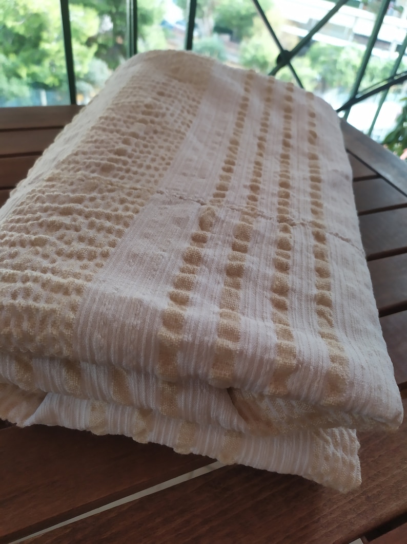 May include: A white and beige striped towel with a textured pattern. The towel is folded in half and is sitting on a wooden surface.