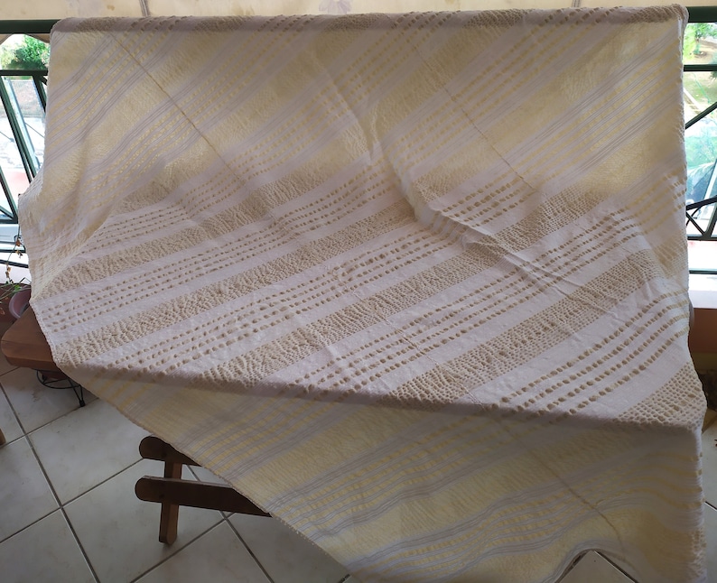 May include: White tablecloth with a yellow and white striped pattern. The tablecloth has a textured surface with small raised dots.