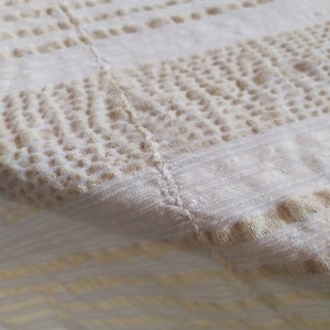 May include: A white tablecloth with a beige pattern of small dots and lines. The tablecloth is made of a soft, woven fabric.