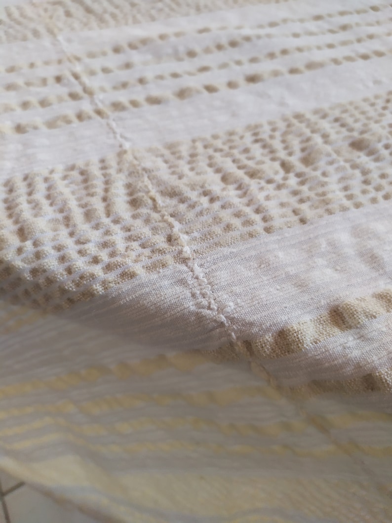 May include: A white tablecloth with a beige pattern of small dots and lines. The tablecloth is made of a soft, woven fabric.