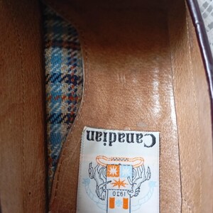 May include: An inside view of a burgundy leather shoe. The interior has a brown leather insole and a patterned fabric lining in blue, orange, and white. A label reads "Canadian 1930" with a graphic.
