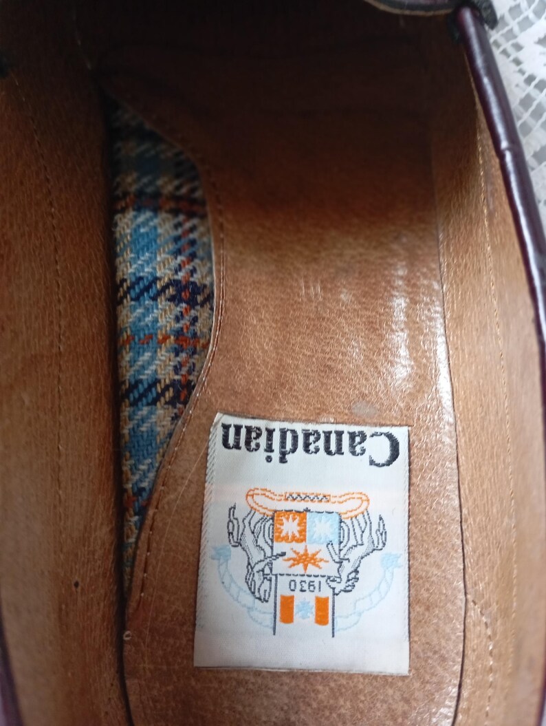 May include: An inside view of a burgundy leather shoe. The interior has a brown leather insole and a patterned fabric lining in blue, orange, and white. A label reads "Canadian 1930" with a graphic.