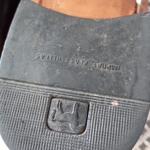 May include: Close-up of a black shoe sole with a ridged texture. The sole has the text "IMPORT PLAST HELLAS" and a logo of a horse inside a square.