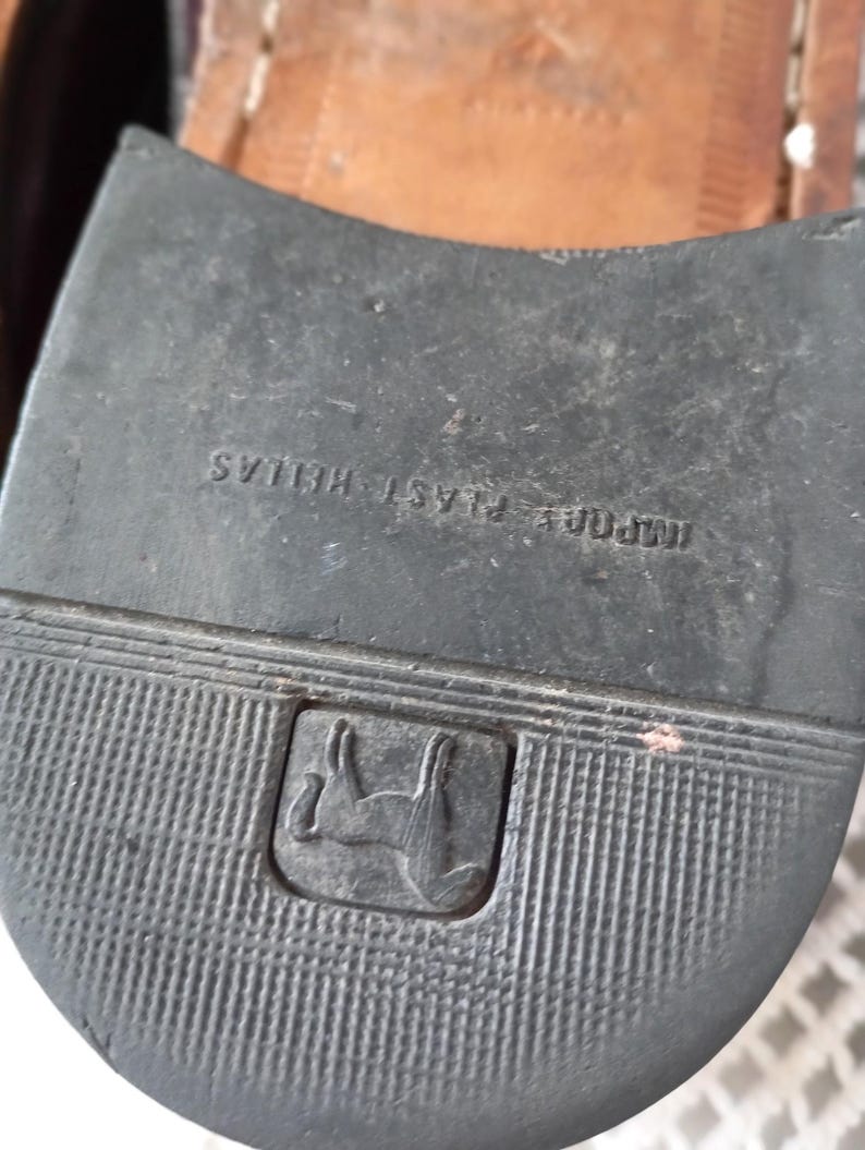 May include: Close-up of a black shoe sole with a ridged texture. The sole has the text "IMPORT PLAST HELLAS" and a logo of a horse inside a square.