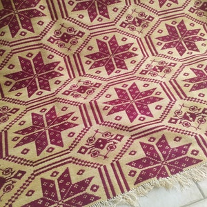 May include: A woven throw blanket with a geometric pattern in shades of burgundy and beige. The blanket has a fringe border.