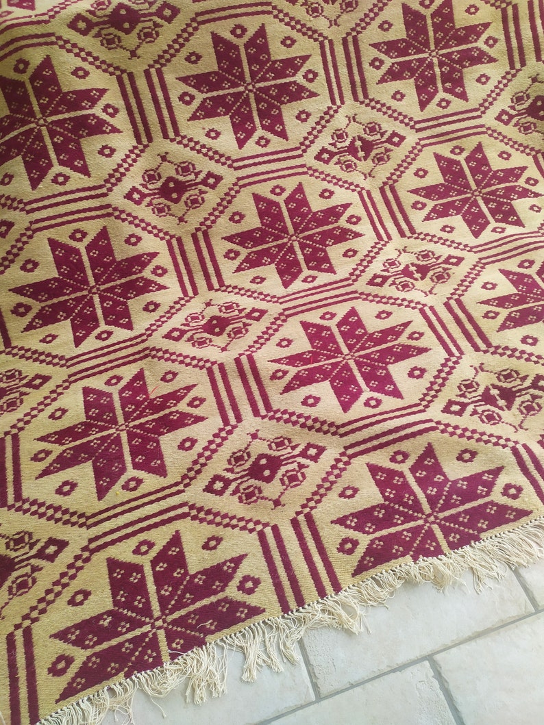 May include: A woven throw blanket with a geometric pattern in shades of burgundy and beige. The blanket has a fringe border.