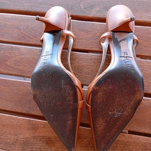 May include: A pair of brown leather heeled sandals with a pointed toe and ankle strap. The sandals have a black leather sole with the text "Made in Italy" and "35" printed on the bottom.