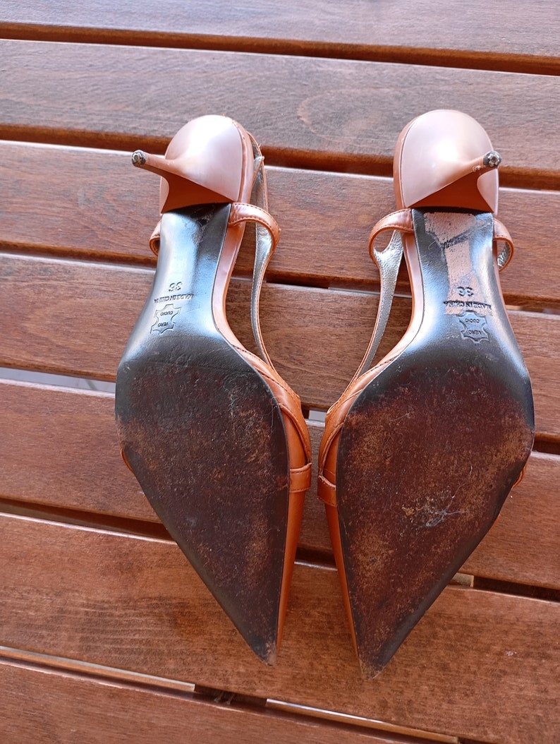 May include: A pair of brown leather heeled sandals with a pointed toe and ankle strap. The sandals have a black leather sole with the text "Made in Italy" and "35" printed on the bottom.