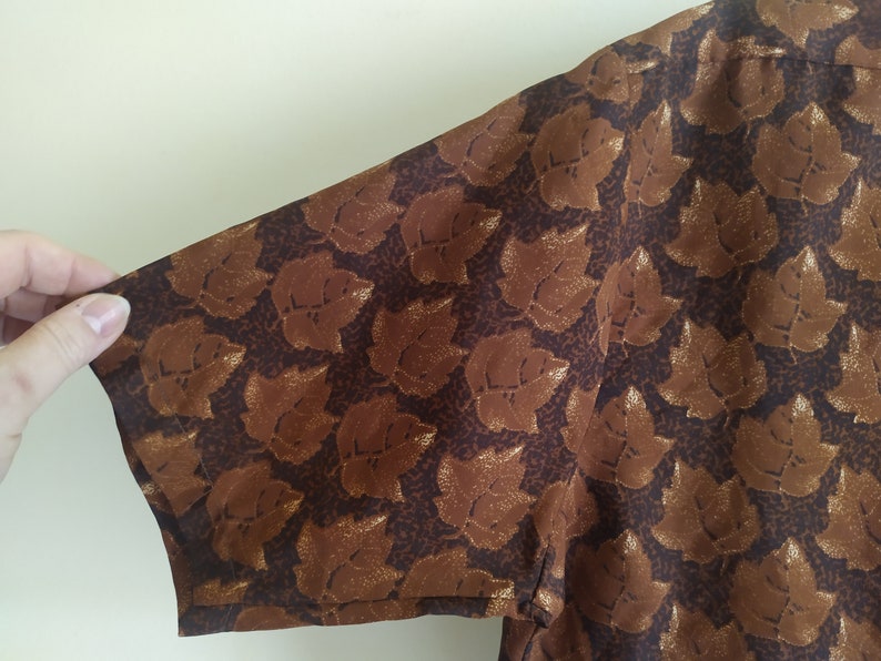 Puede incluir: Una camisa marr&oacute;n de manga corta con un estampado de hojas doradas.