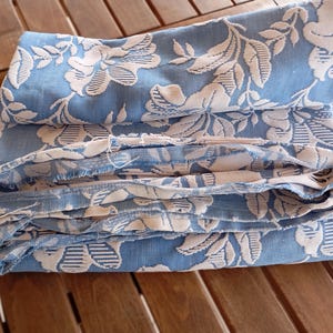 May include: A stack of blue and white fabric with a floral pattern. The fabric is folded and has a frayed edge.