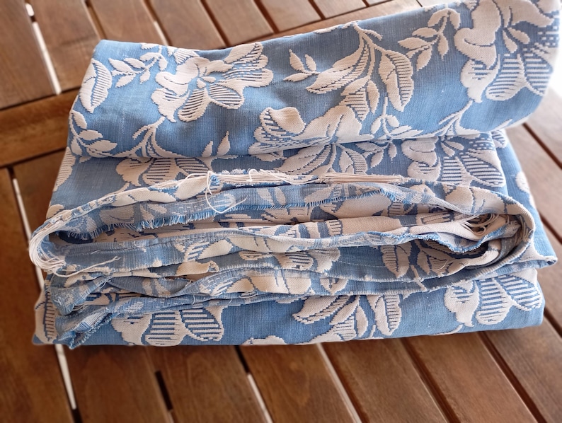 May include: A stack of blue and white fabric with a floral pattern. The fabric is folded and has a frayed edge.