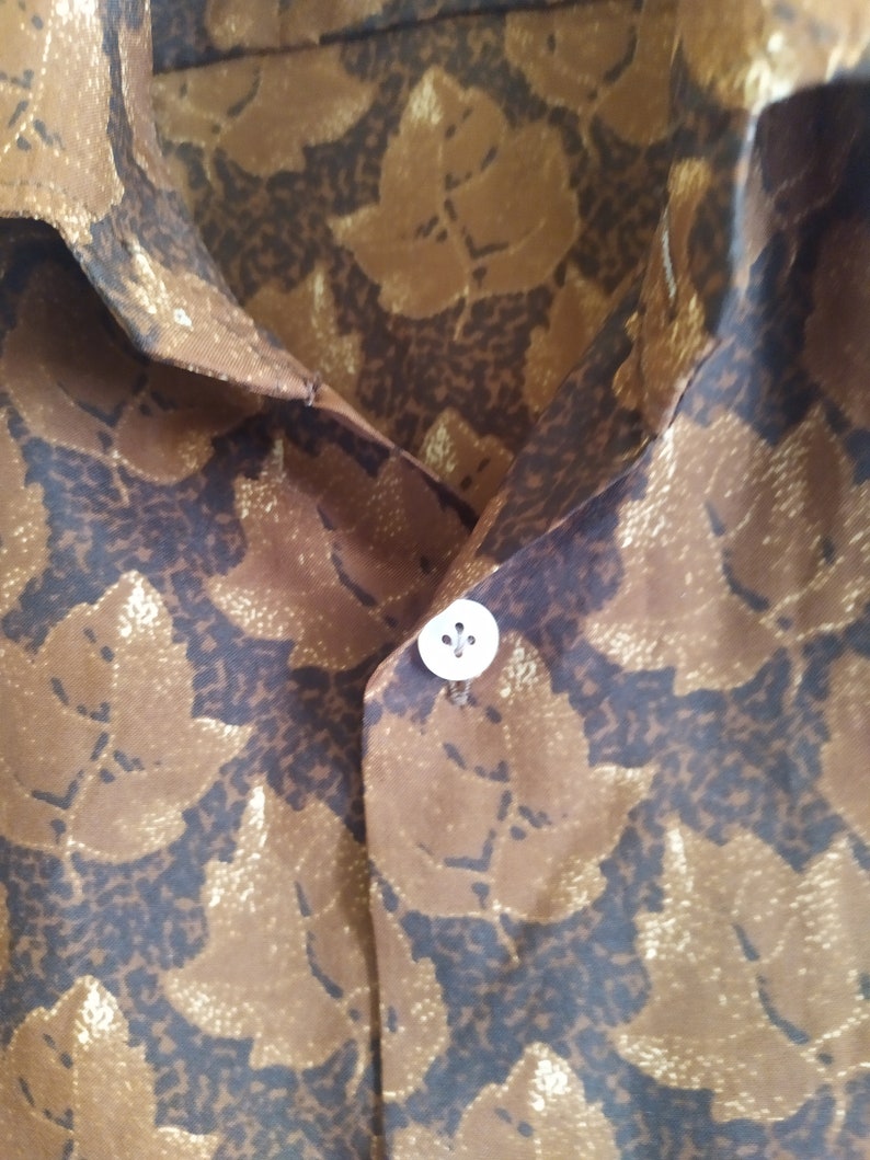 Puede incluir: Una camisa de color marr&oacute;n y dorado con un bot&oacute;n blanco.