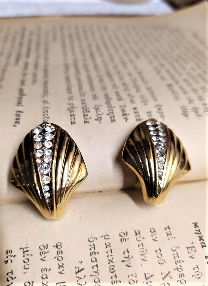 May include: A pair of gold tone clip-on earrings with a shell design and clear rhinestones.