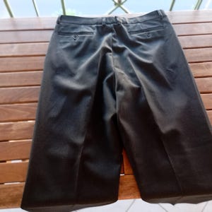 May include: A pair of black trousers featuring a waistband with belt loops, a centre front zip closure, and two back pockets with button closures. The trousers have a straight-leg cut with a visible crease running down the centre of each leg.