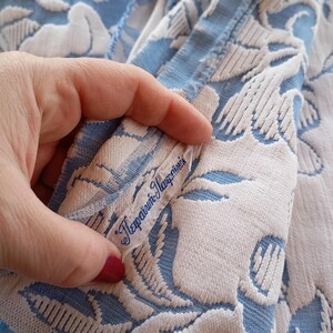 May include: A close-up of a blue and white fabric with a floral pattern. The fabric has a label that reads "Tefraini-Marzolini".