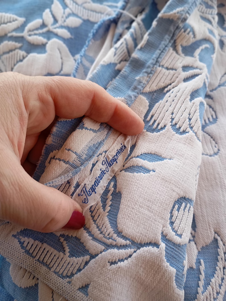 May include: A close-up of a blue and white fabric with a floral pattern. The fabric has a label that reads "Tefraini-Marzolini".