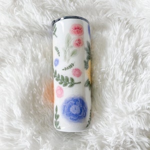 Op de afbeelding: Een witte roestvrijstalen beker met een bloemenontwerp met roze, blauwe, gele en groene bloemen.