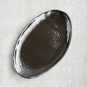 May include: A black oval ceramic serving platter with a white rim and a geometric pattern.