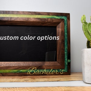 May include: A wooden picture frame with a green and yellow resin inlay. The frame has a black background and the text "Bachelor's" is written in gold lettering at the bottom. The text "Custom color options" is written in white lettering on the frame.