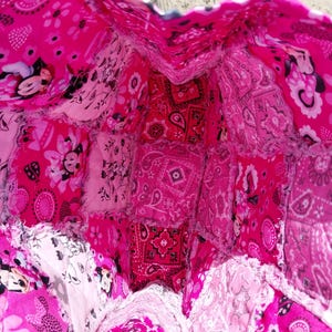 Puede incluir: Un bolso tote patchwork hecho a mano en tonos rosas. El bolso presenta una variedad de telas estampadas, incluyendo estampados de cachemira, florales y de Mickey Mouse. El interior es visible, mostrando la construcci&oacute;n del bolso y los diferentes trozos de tela utilizados.