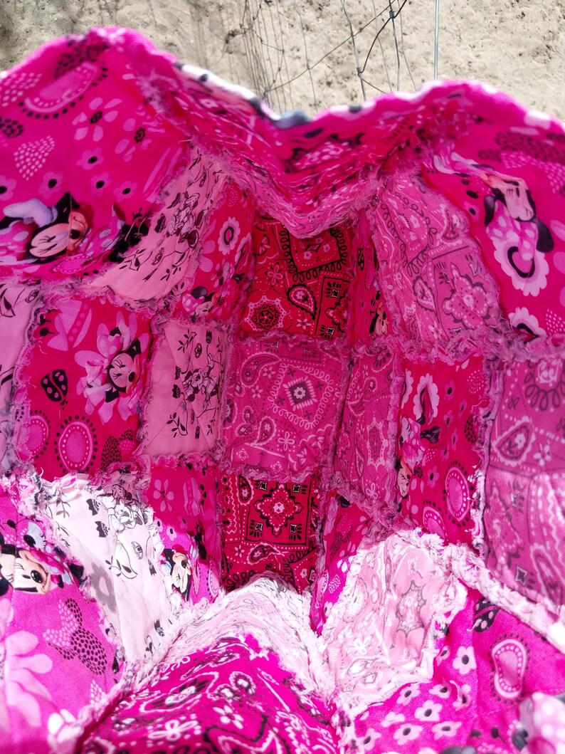 Puede incluir: Un bolso tote patchwork hecho a mano en tonos rosas. El bolso presenta una variedad de telas estampadas, incluyendo estampados de cachemira, florales y de Mickey Mouse. El interior es visible, mostrando la construcci&oacute;n del bolso y los diferentes trozos de tela utilizados.