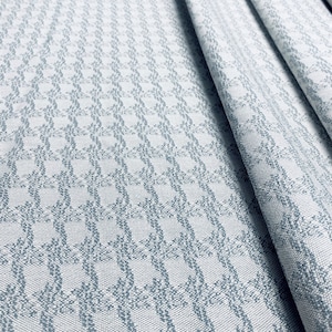 May include: A white fabric with a blue geometric pattern. The fabric is folded and has a textured surface.