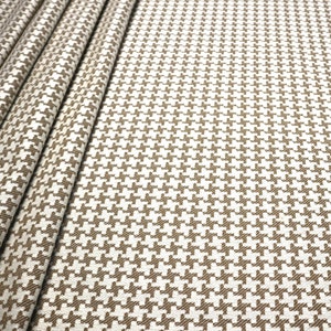 May include: Brown and white houndstooth fabric with a subtle texture. The fabric is folded in a few places, showing the pattern from different angles.
