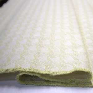 May include: A close-up of a folded piece of fabric with a light green and white geometric pattern. The fabric has a slightly frayed edge.