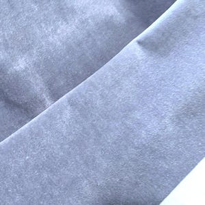 May include: A close-up shot of a folded piece of light blue fabric. The fabric has a soft, velvety texture and a subtle sheen. The folds create diagonal lines across the image, highlighting the fabric's drape.
