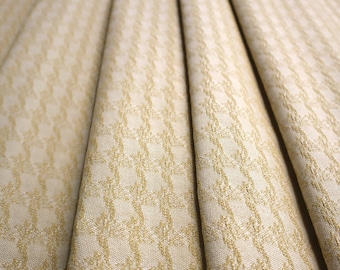 May include: Close-up of a beige fabric with a subtle gold geometric pattern. The fabric is folded in a fan shape, showcasing the texture and design.