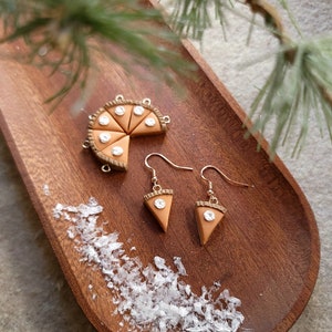 May include: A pair of dangle earrings with a brown pie slice charm and a clear rhinestone. The earrings are displayed on a wooden tray with a brown pie slice charm.