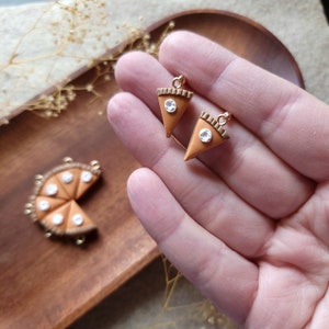 May include: Two gold-rimmed pie slice charms with white filling and a gold accent. A whole pie charm with white filling is also visible in the background.