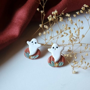 May include: A pair of handmade polymer clay earrings featuring a white ghost on a brown pumpkin with green leaves.