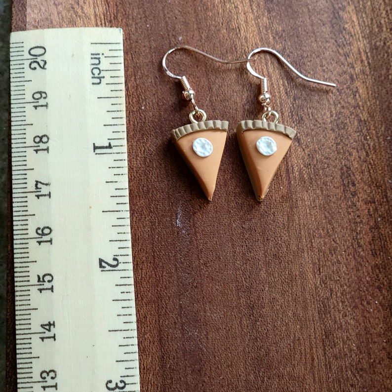May include: A pair of gold dangle earrings with a brown pie slice charm. Each pie slice has a white pearl-like center.