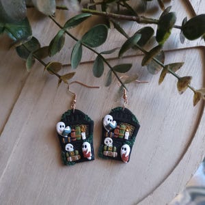 May include: A pair of black and green Halloween-themed earrings featuring a tombstone with ghosts and books. The tombstone has the word "RIP" on it.