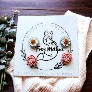 May include: A set of three handmade polymer clay earrings featuring a floral design. The earrings are displayed on a white card with the text "Handmade Jewelry Foxy Method Custom Designs & More".