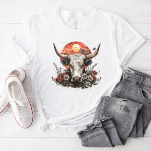 May include: White t-shirt with a graphic of a white bull's head with horns, surrounded by flowers and a red sunset.
