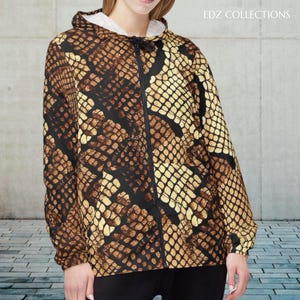 Pode incluir: Casaco com capuz com padrão de pele de cobra em tons de castanho, preto e bege. O casaco tem um fecho de correr comprido e um capuz com cordão. O texto "EDZ COLLECTIONS" é visível no canto superior direito.