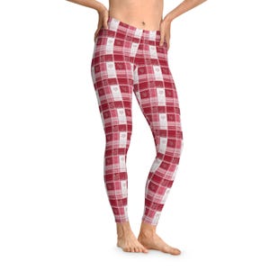 May include: Red and white plaid leggings with a patchwork design. The leggings feature a mix of patterns, including squares, snowflakes, and floral motifs. The color scheme is predominantly red and white, creating a festive and cozy look.