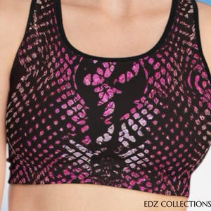 Puede incluir: Un sujetador deportivo negro con un estampado de piel de serpiente rosa y blanco. El sujetador tiene cuello redondo y ribete negro. El texto "EDZ COLLECTIONS" está en la parte inferior de la imagen.