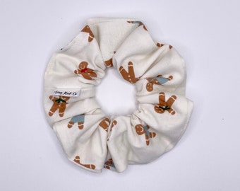 May include: A white scrunchie with a gingerbread man pattern. The scrunchie has a small tag that says "Amy Knit Co."
