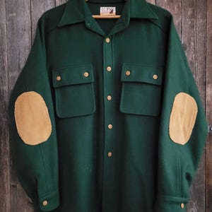 May include: A dark green long-sleeve shirt featuring a pointed collar, a front button closure, and two chest pockets with buttoned flaps. The sleeves include tan corduroy elbow patches, and the interior label displays the text Lobo.