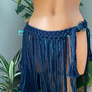 May include: A navy blue crochet skirt with long fringe. The skirt is tied at the waist with a braided rope and has a metal ring closure.