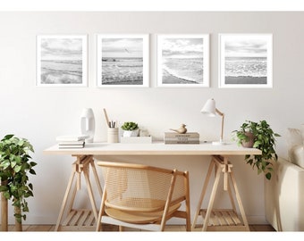 May include: Four black and white framed photographs of ocean waves and a beach scene hang on a white wall above a wooden desk with a chair. The desk has a white surface and is supported by two wooden sawhorses. There are books and a lamp on the desk.