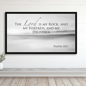 May include: Black and white framed wall art with a quote from Psalms 18:2, "The Lord is my rock, and my fortress, and my deliverer." The background is a blurry image of a beach.