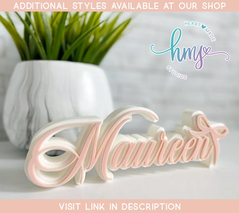 May include: A white and pink 3D name sign that says "Maureen" in a cursive font. The sign is made of a lightweight material and is perfect for a shelf or mantle.